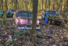 Verlassene, rostige Oldtimer auf einem Waldfriedhof.
