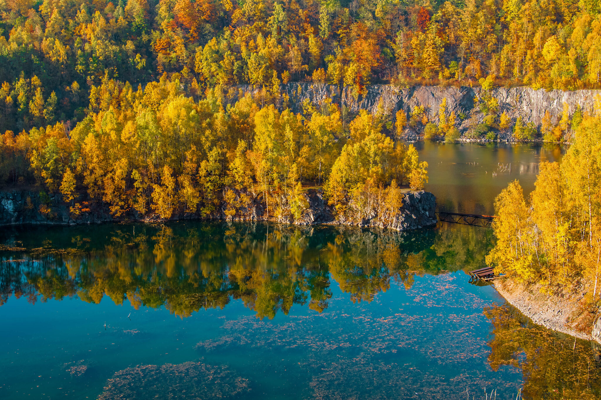 Goldener Herbstwald spiegelt sich im klaren Wasser des Steinbruchs.