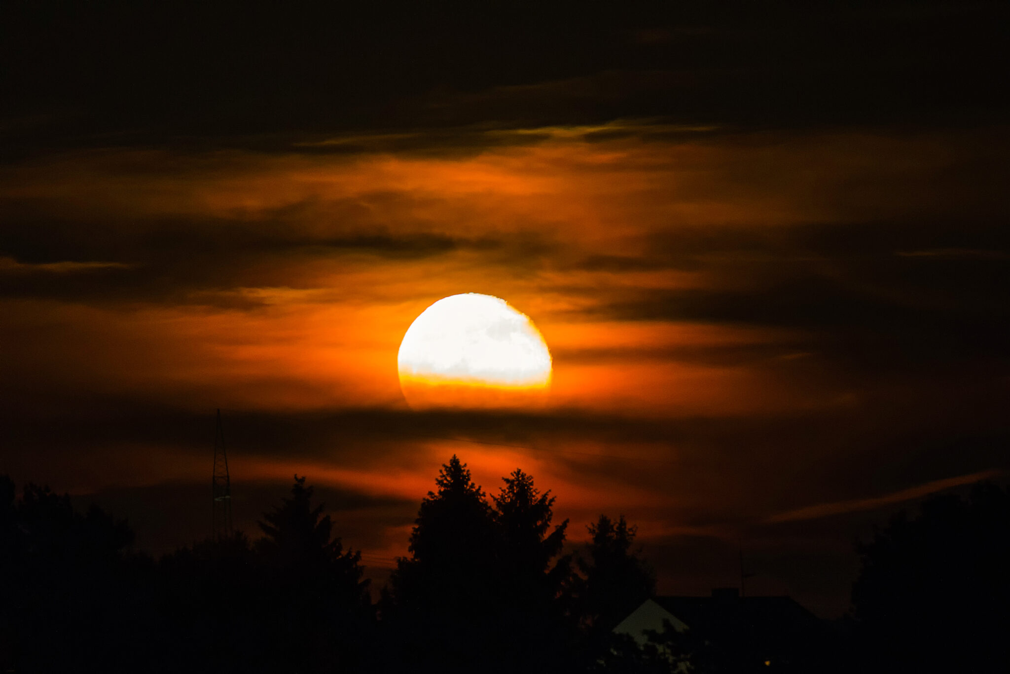 Feuriger Mondaufgang über den Silhouetten der Bäume.